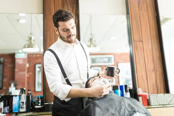 专业英俊的理发师在商店的客户脸上应用剃须泡沫 — 图库照片