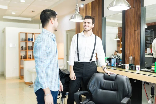 微笑的年轻理发师提供座位给顾客在沙龙 — 图库照片