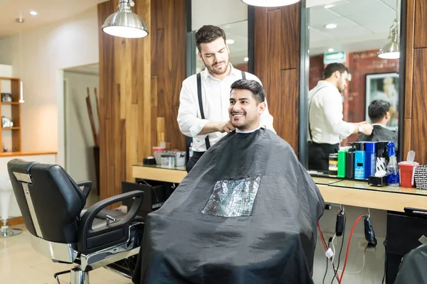 年轻理发师调整海角在微笑的顾客在沙龙 — 图库照片