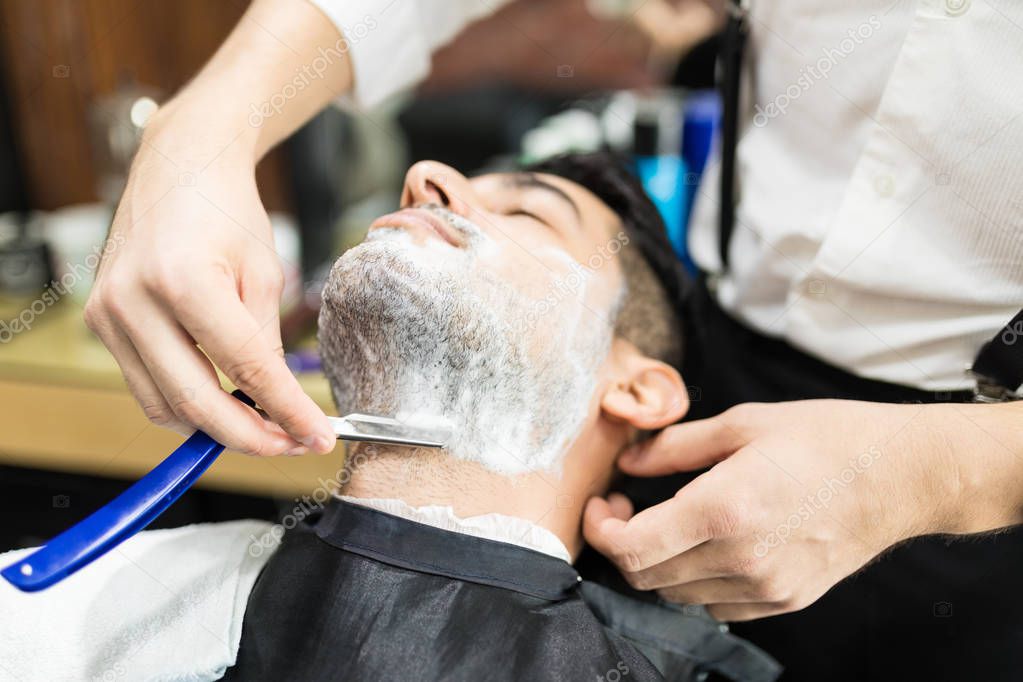 Closeup of barber hands shaving man's stubble with straight razors at shop
