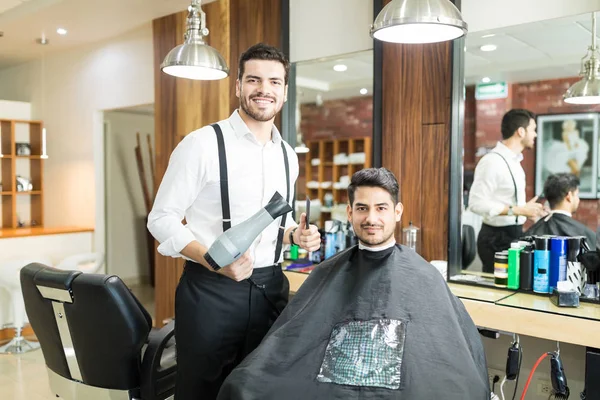 年轻理发师的肖像与吹风机站在男性客户附近的新发型沙龙 — 图库照片