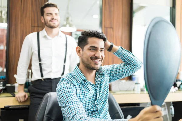 满意的男性客户看手持镜后发型与美发师在商店背景 — 图库照片