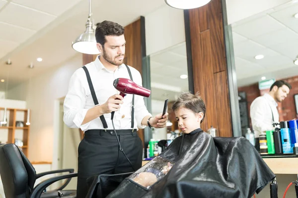 自信的年轻理发师在理发店里干头发的男孩子 — 图库照片