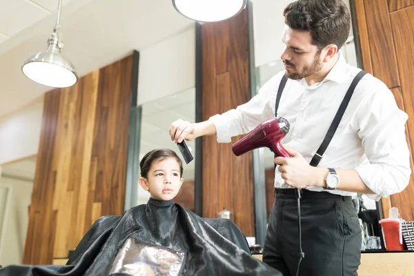 Молодий Перукар Тримає Сушарку Під Час Розчісування Волосся Хлопчика Салоні — стокове фото