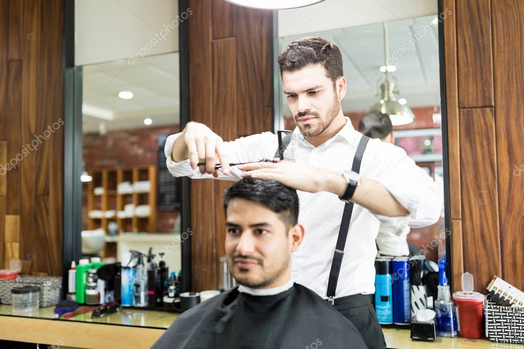 Confident hairstylist focusing on cutting hair of customer to give him trendy look in salon
