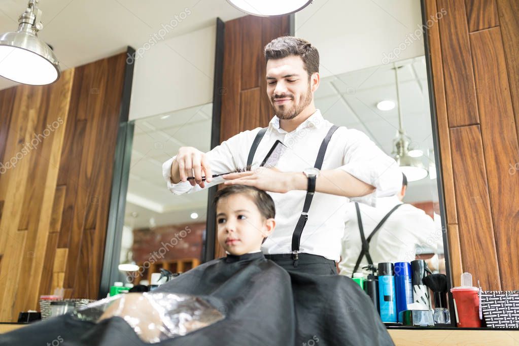 Cute little boy is getting haircut by male hairdresser at the barber shop