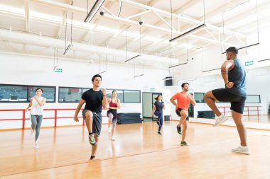 Erkek eğitmen ve spor salonunda aerobik getirirken yüksek diz çalışan iş istemciler