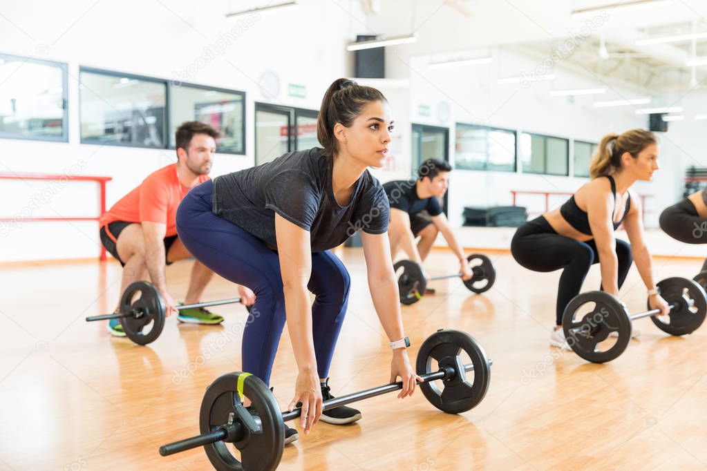 Female weightlifter lifting barbell while doing lunges with friends in health club