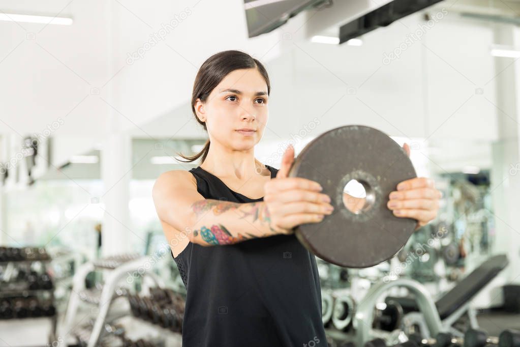 Confident young woman exercising with barbell plate during gym class