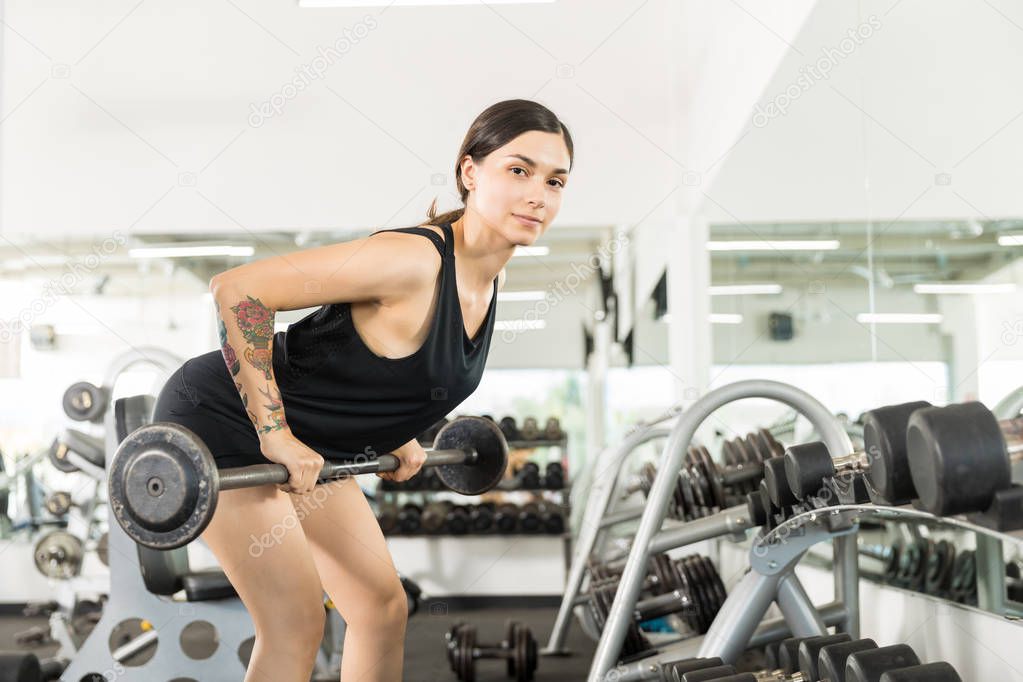 Determined athlete doing bent over row exercise with barbell in gym