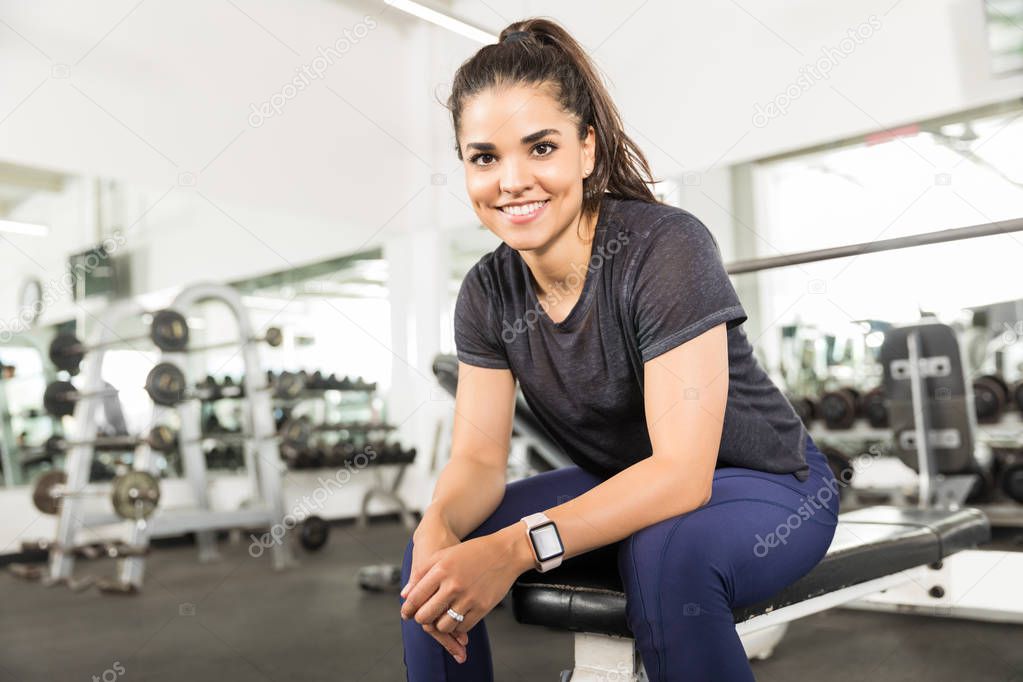 Portrait of smiling healthy female sitting on bench in fitness center