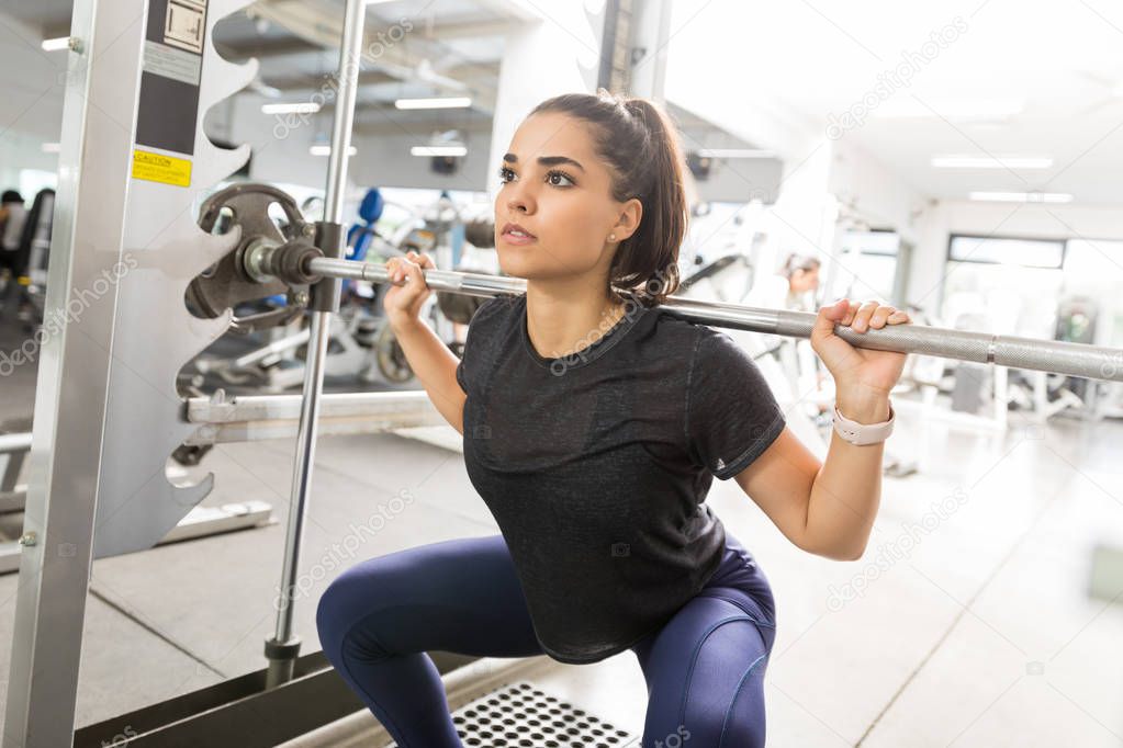 Focused female athlete doing barbell squats in gym