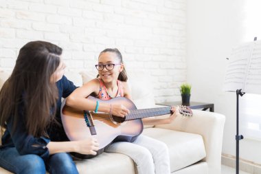 Kadın öğretmen kız evde kanepede otururken gitar çalmayı öğretim