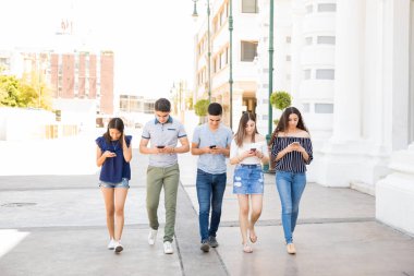 Açık havada yürüyüş ve telefonlarını kullanarak İspanyol Genç çocukların kaldırmalı ve kız grubu