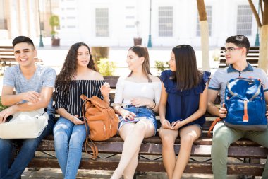 Latin gençler açık havada bankta oturan ve bahsediyorsun sırt çantaları ile portresi