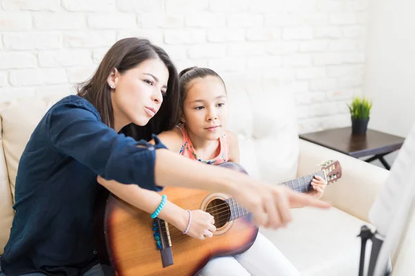 女性の家庭教師が家でギターを弾いている女の子に音符を表示 — ストック写真