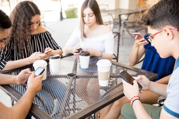 一群十几岁的朋友在他们的智能手机上更新他们的社交媒体状态 而坐在街头咖啡馆 Tabl — 图库照片