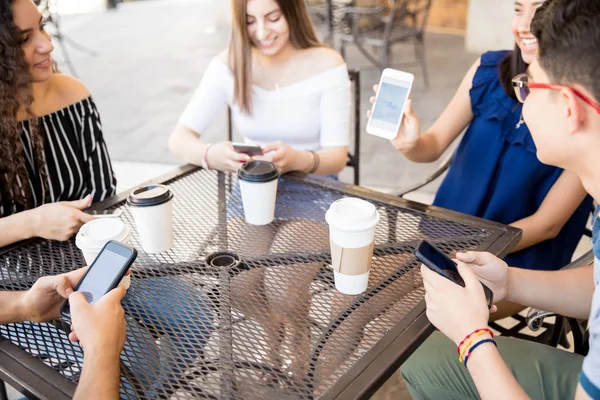 年轻女孩在她的智能手机上显示一幅图片给她的朋友 而在户外咖啡馆喝咖啡 — 图库照片