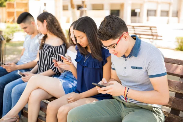 年轻的男孩与朋友使用智能手机坐在长凳上户外 — 图库照片