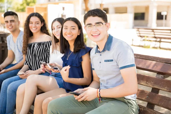 Göz Teması Yapma Gülümseyen Telefonlarla Bankta Takılmak Beş Latin Genç — Stok fotoğraf