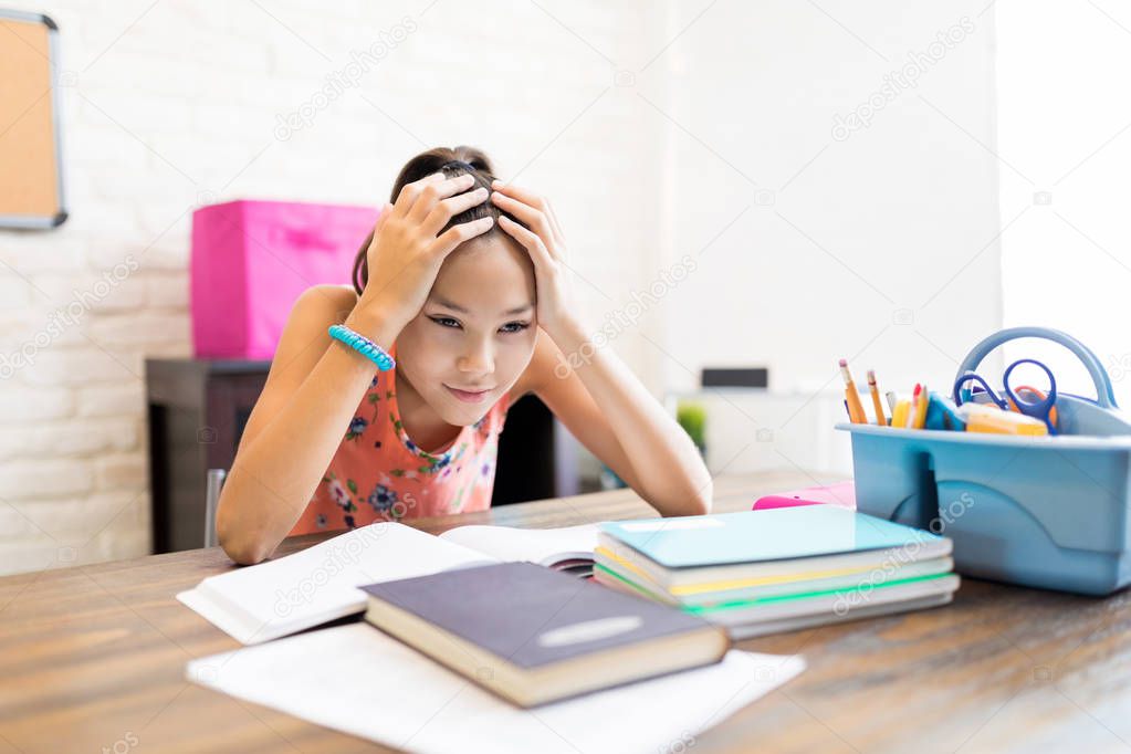 Stressed female student with head in hands sitting at table in house