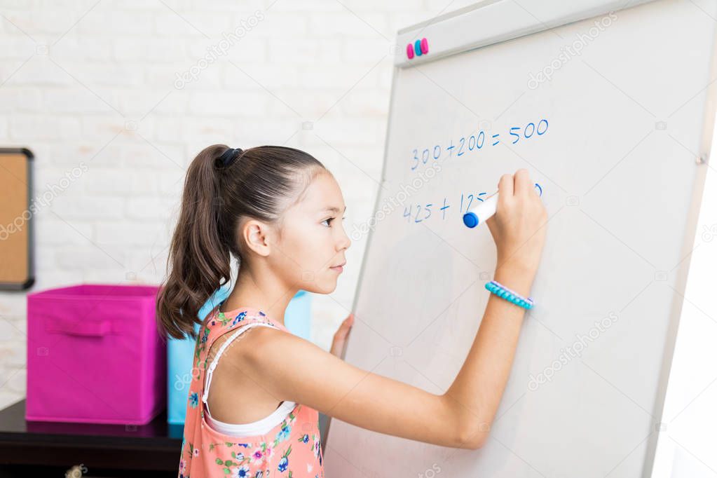 Side view of confident girl solving math's sums on flip chart at home