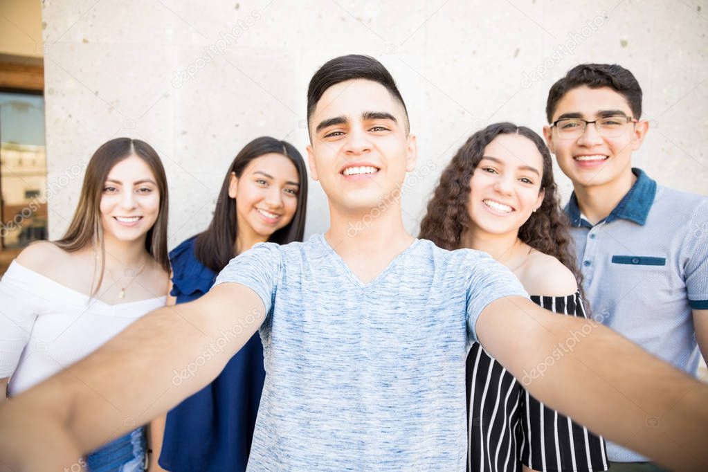 Teenage boy taking selfie with friends on smartphone while hanging out in cit