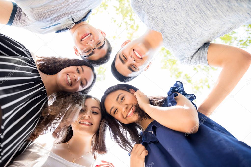 Low angle view of group of teenagers standing in a huddle with their heads touching and looking at camera