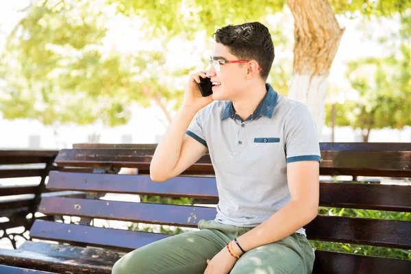 Portrait of hispanic boy sitting on bench outside talking on mobile phone