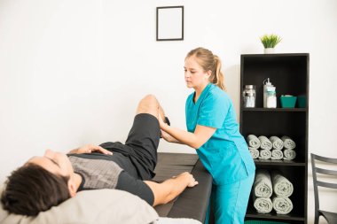 Bacak egzersiz hastanede ile erkek atlet yardımcı genç kadın fizyoterapist