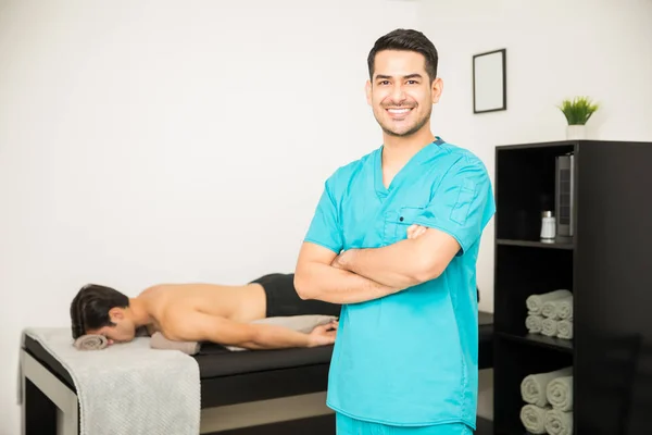 Smiling Fisioterapeuta Masculino Pie Brazos Cruzados Con Paciente Acostado Fondo — Foto de Stock