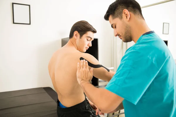 Terapeuta Masculino Aplicando Fita Terapêutica Elástica Ombro Homem Sem Camisa — Fotografia de Stock
