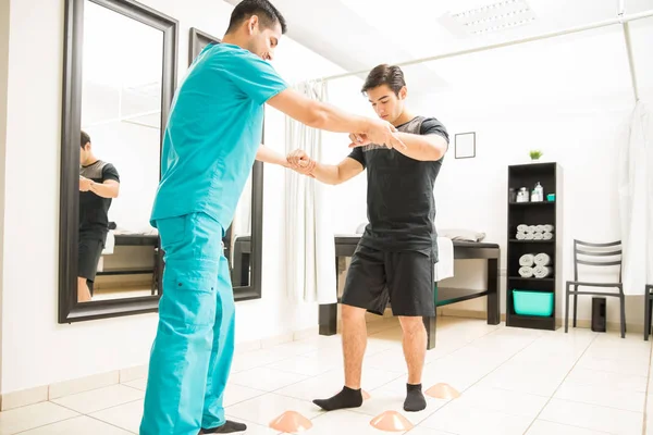 青年理疗师帮助运动员在医院的锥间行走 — 图库照片
