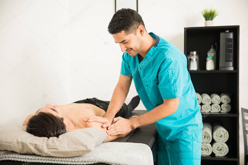 Male physical therapist massaging the injured shoulder of male athlete in hospital