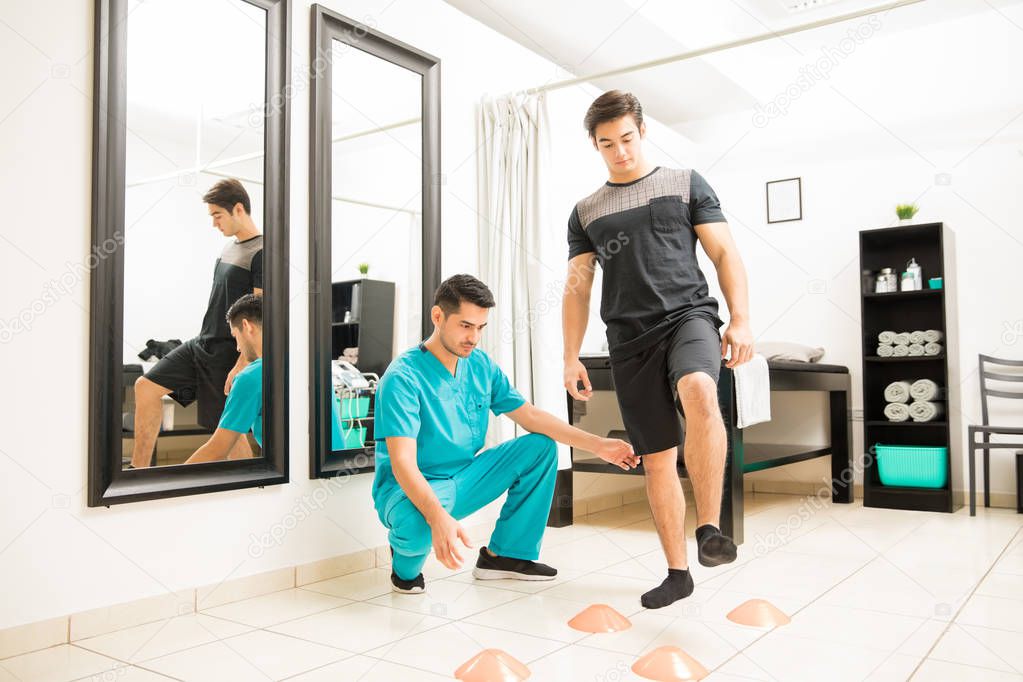 Physical therapist motivating male patient to walk between cones in hospital