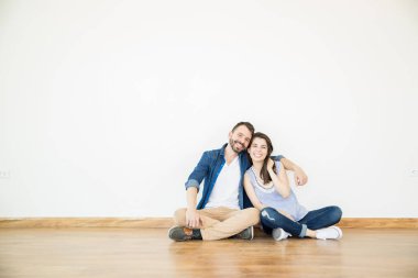 Yeni daire içinde beyaz duvara otururken gülümseyen kadın ve erkek portresi