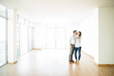 Full length of mid adult man kissing woman on cheek in new apartment clipart