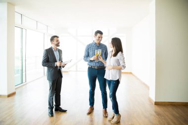 Real estate agent looking at couple celebrating with champagne toast in new apartment clipart