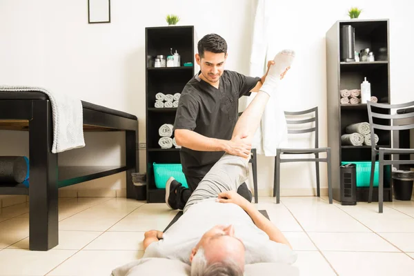 Jovem Fisioterapeuta Ajudando Homem Maduro Com Exercício Perna Clínica Reabilitação — Fotografia de Stock