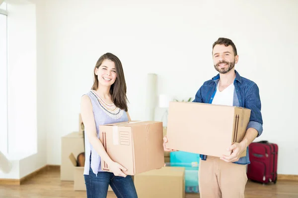 Portrait of satisfied couple carrying corrugated boxes while moving to new house
