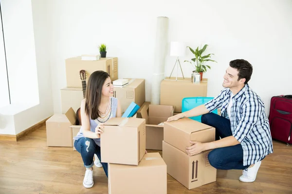 Happy man and woman in casuals crouching while stacking cardboard boxes in new home