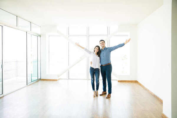 Smiling mid adult couple standing arms outstretched in new apartment