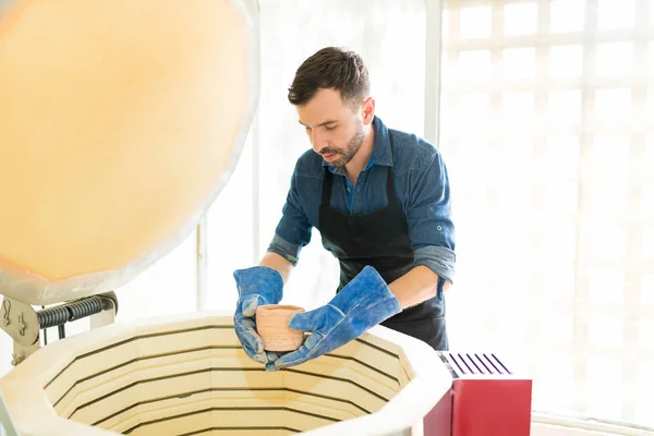 中成年男子戴手套 而在陶器工作室放置粘土杯入窑 — 图库照片