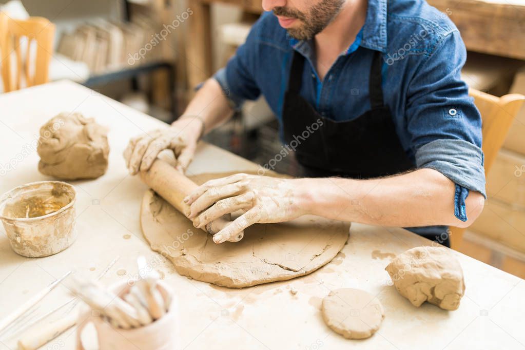 Midsection of mid adult man flattening the clay with rolling pin in pottery class