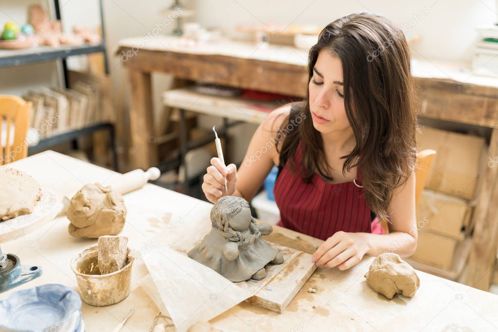 Beautiful female artisan making pottery of doll at table in studio