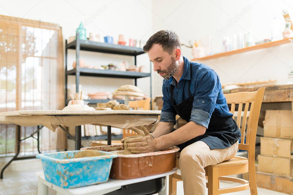 Mid adult male potter creating creative pottery while sitting in workshop