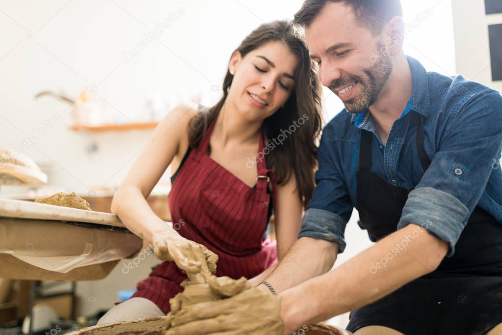 Man and woman working on potter wheel while on date at pottery workshop