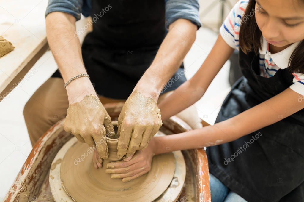 Hands of teacher and girl shaping clay on pottery wheel in studio