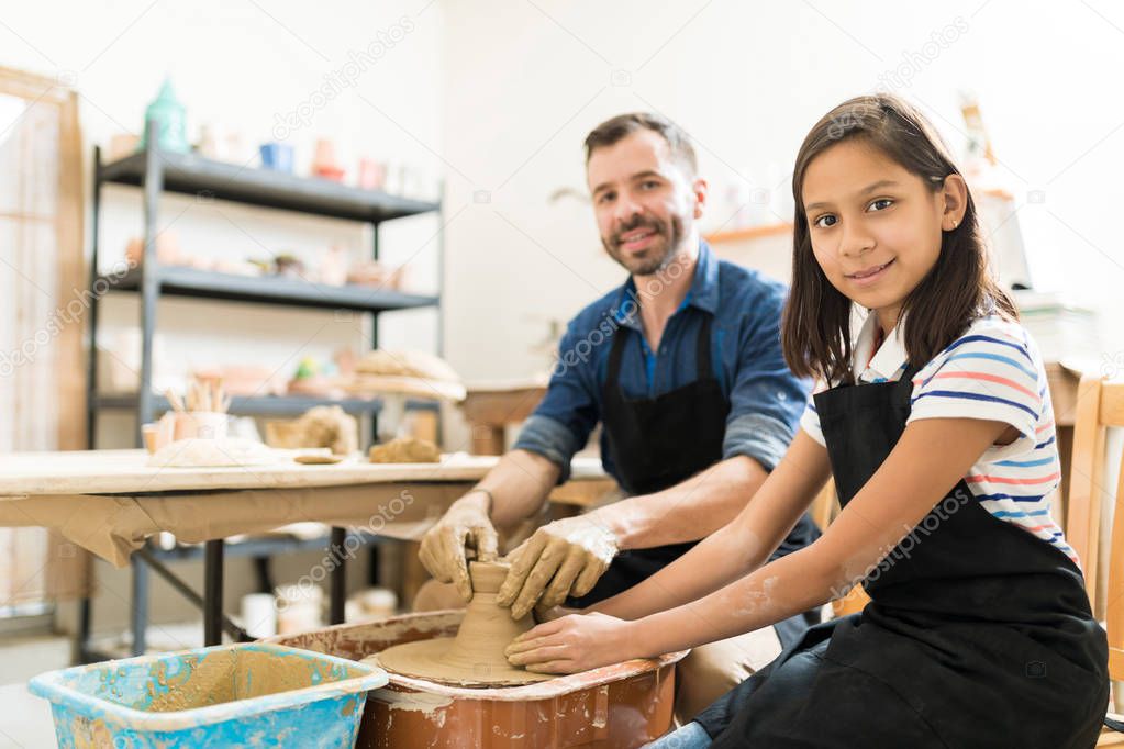 Smiling preteen girl learning pottery from teacher in workshop