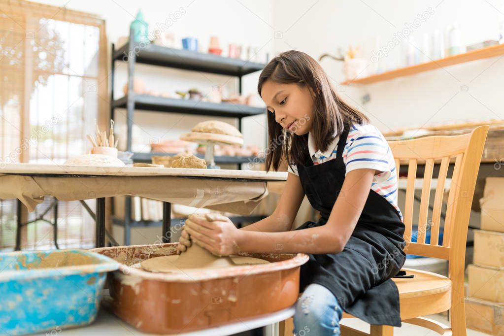 Creative girl manufacturing clay product on pottery wheel at workshop